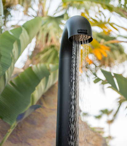Outdoor shower that is turned on with palm leaves behind