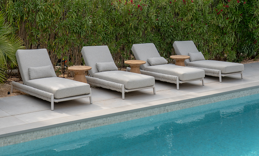 Four beige sun beds in front of swimming pool with wooden side tables
