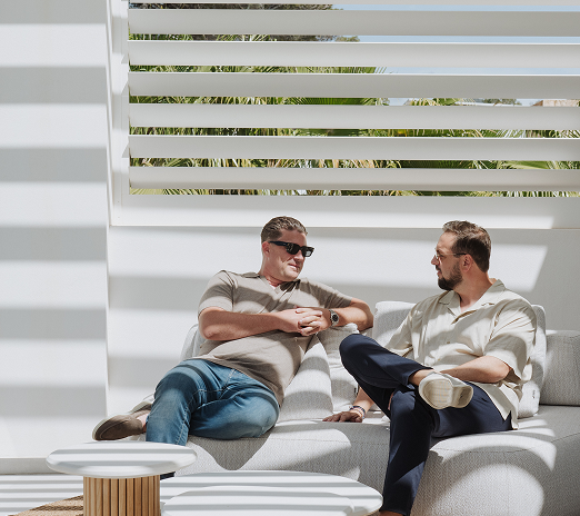 Two men having a conversation on a white outdoor sofa under modern pergola