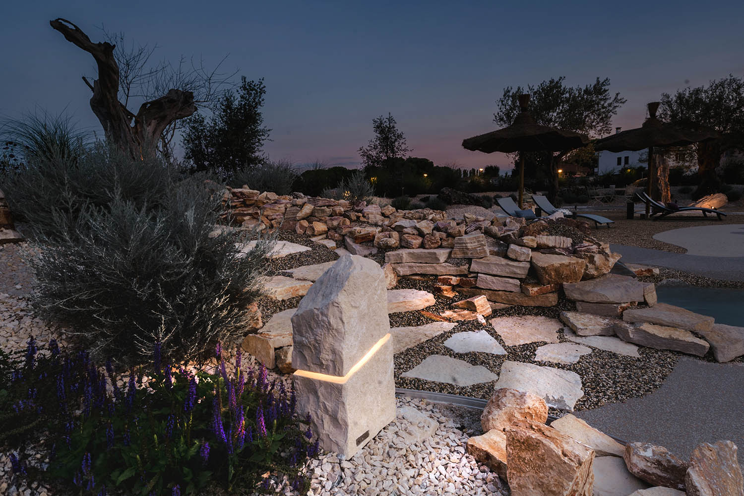 Natural garden lighting Menhir di Luce bij dusk, surrounded by stones and plants