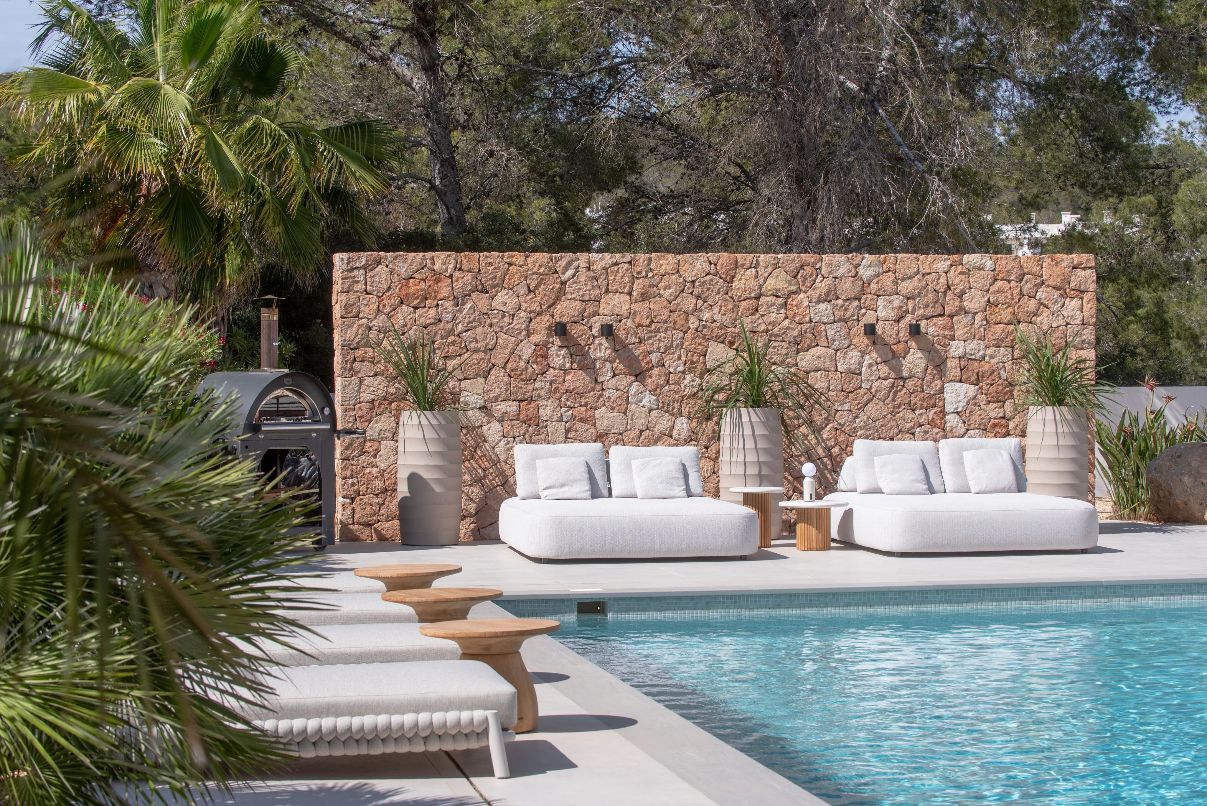 Two designer daybeds next to a natural stone wall by the pool