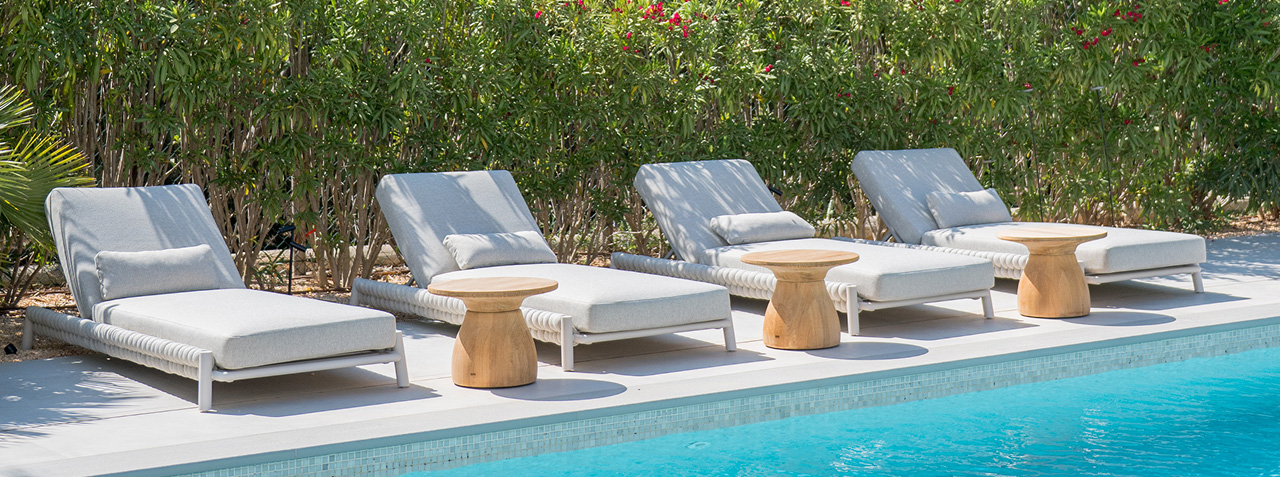 Luxury sun loungers with wooden side table by a modern pool.