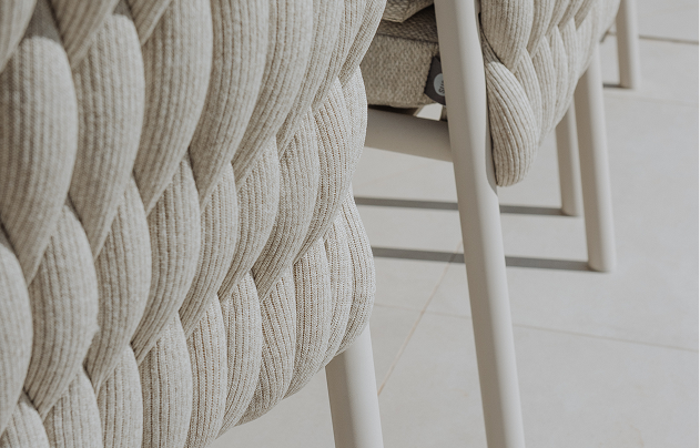 Close-up of woven upholstered outdoor dining chair with white legs.